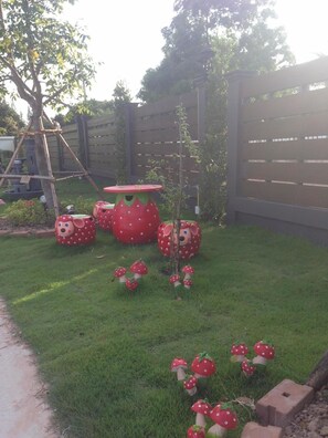 Un jardín con un columpio de madera, un pequeño árbol y varias decoraciones con forma de hongo.