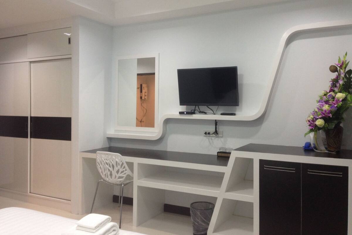 A modern hotel room with a bed, a desk, a TV, a mirror, and a wardrobe.