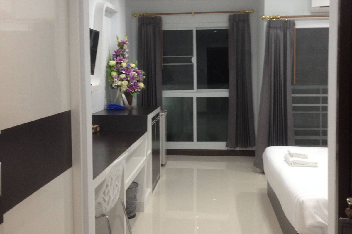 A modern hotel room with a bed, a desk, and a window with curtains.