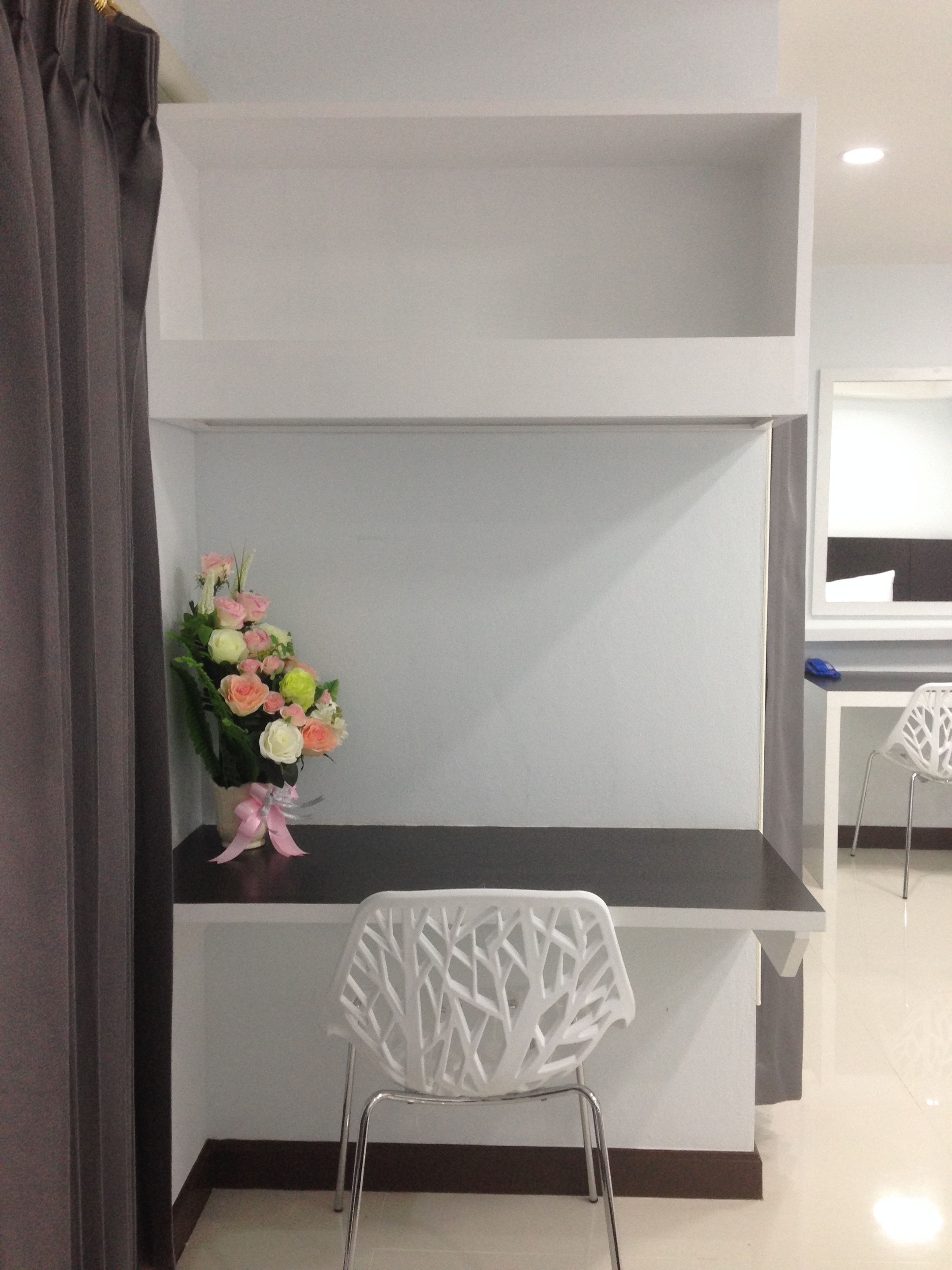 Een moderne kamer met een wit bureau, een witte stoel en een bloemenvaas.