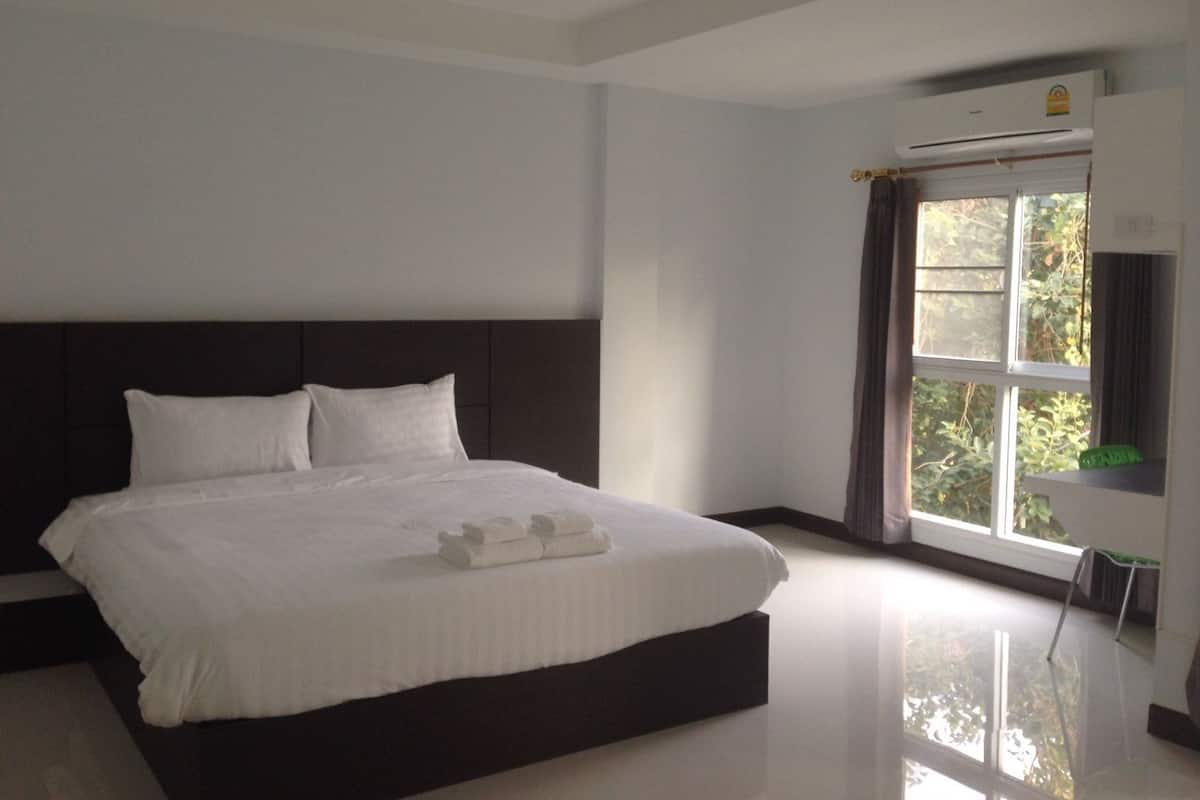A modern bedroom with a large bed, a window with curtains, and an air conditioning unit.