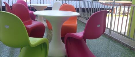 Un patio con sillas de plástico de colores y una mesa blanca.