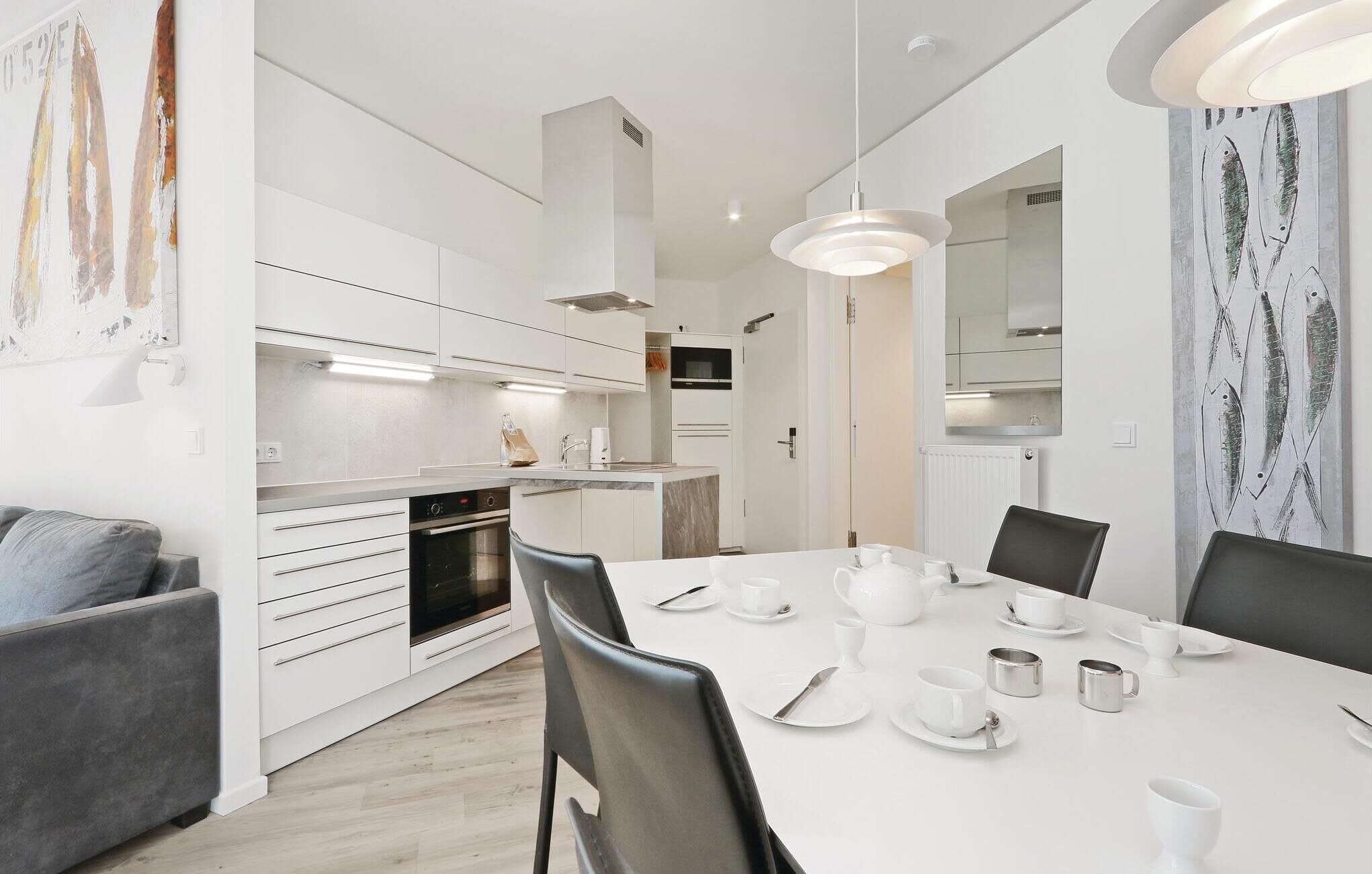 A modern kitchen with white cabinetry, a built-in oven, and a dining area with a white table set for four.