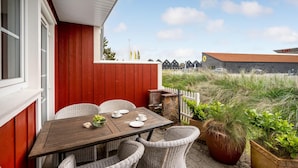 En terrasse med et bord dækket til to, fletstole og en potteplante.