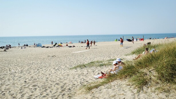 En strand med folk, der solbader og går en tur.