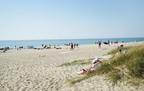 Uma praia com pessoas tomando sol e caminhando.