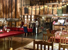 Un interior rústico con paredes de madera, mesas con manteles rojos y luces de cuerda.