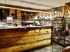Zona de bar con estanterías de madera, mostrador y jaula de pájaros.