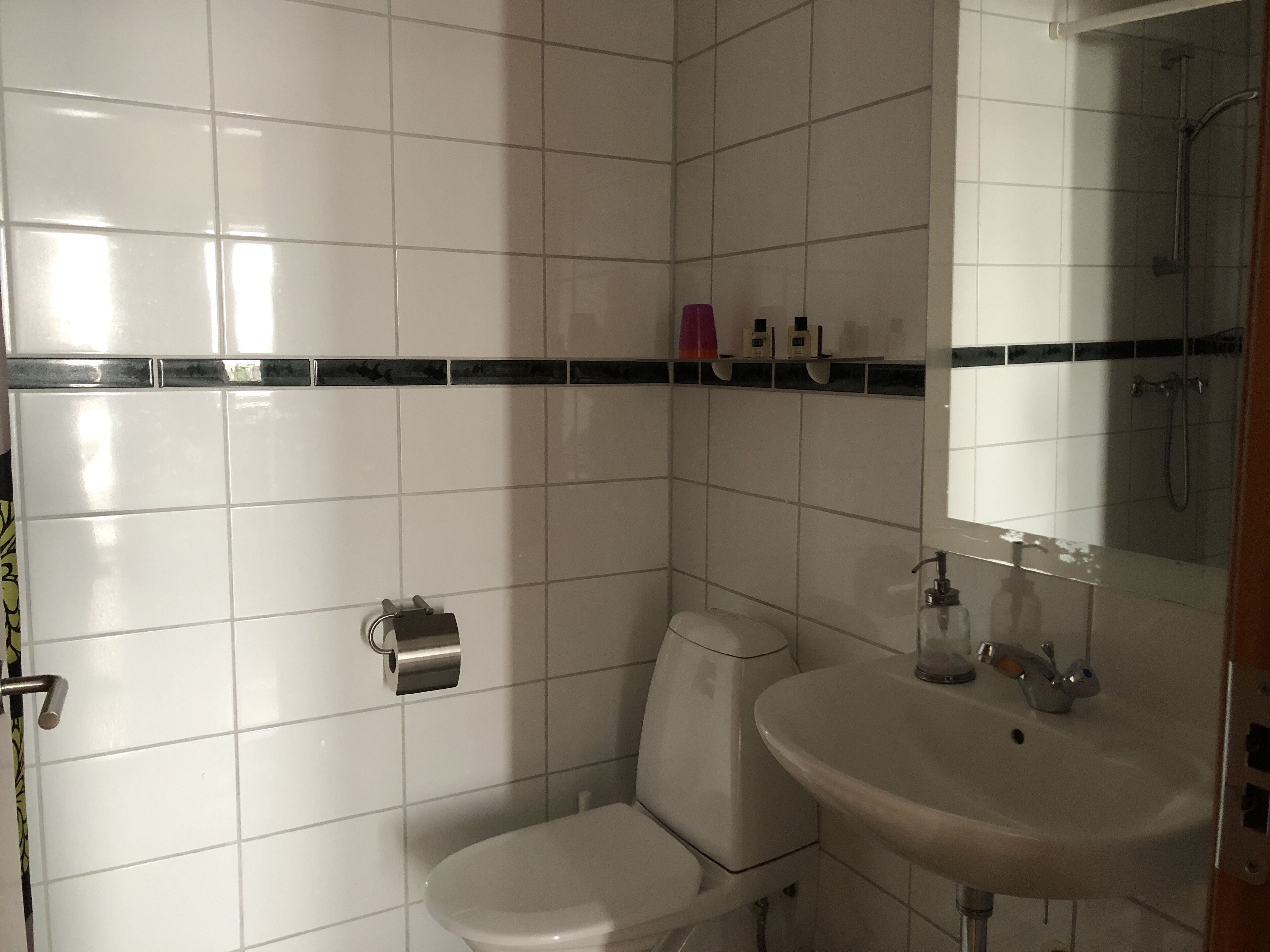 Un baño con azulejos blancos, inodoro, lavabo y ducha.