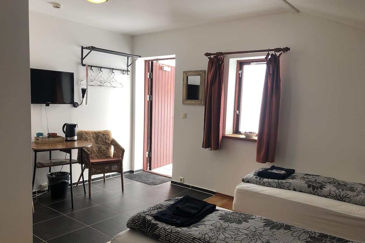 A compact room with a bed, a chair, a table with a kettle, and a TV mounted on the wall.