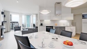 A modern kitchen with white cabinets, a dining area with a white table set for four, and a large window providing a view of the city.