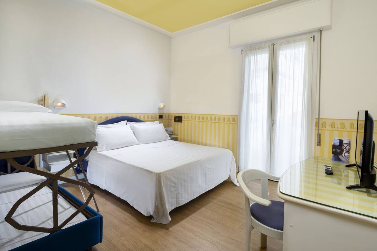 A hotel room with two beds, a desk with a chair, and a television.
