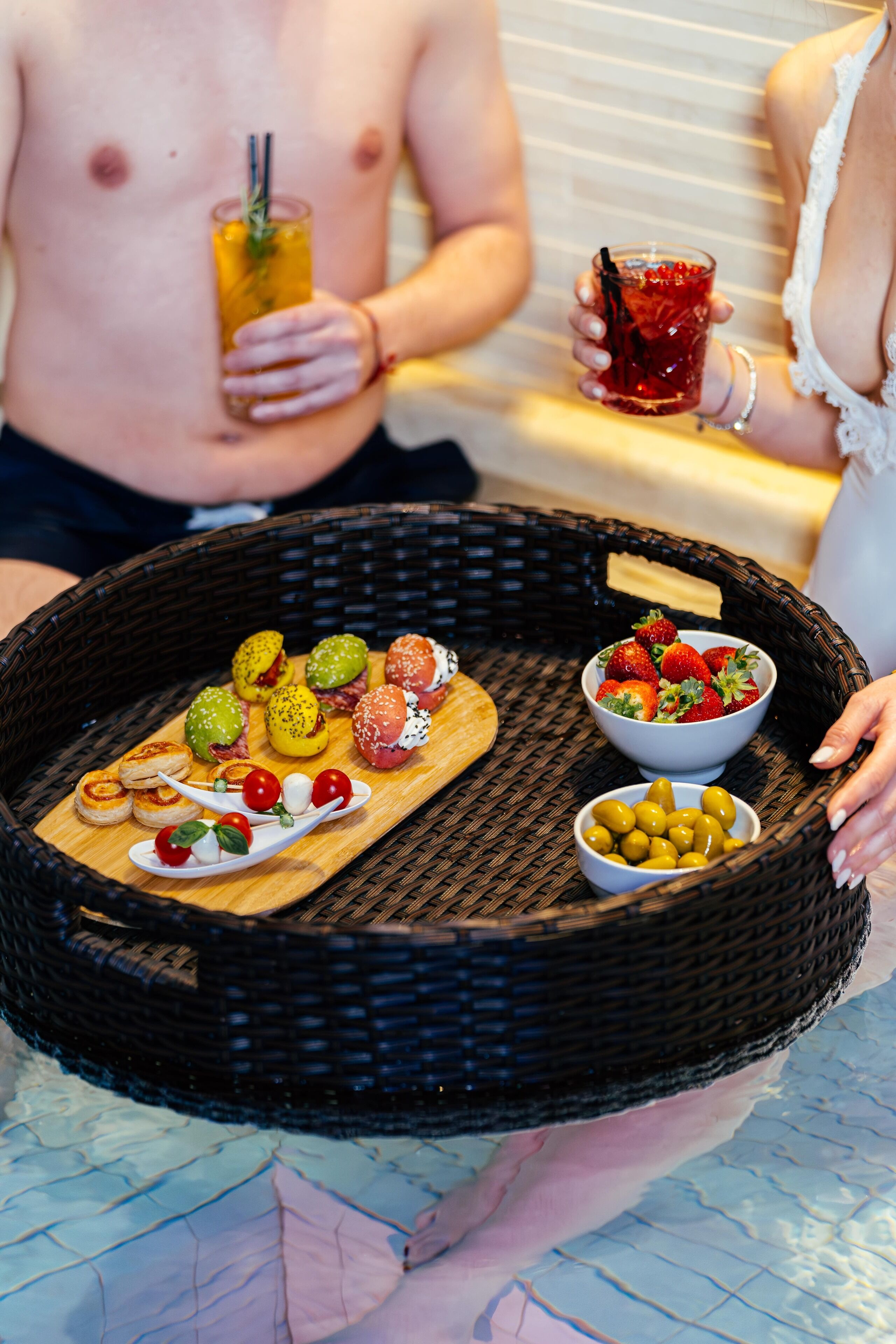 A wicker tray with food and drinks, including strawberries, olives, and a drink with a straw.
