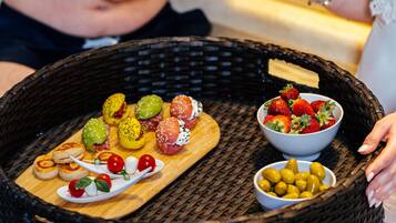 A wicker tray with food and drinks, including strawberries, olives, and a drink with a straw.