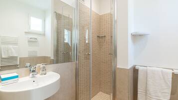 Un baño moderno con ducha de vidrio, lavabo blanco y un perchero para toallas.