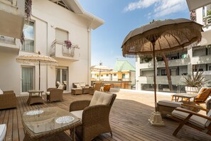 A wooden deck with wicker furniture, a glass table, and a large umbrella. - Hotel Estense (Gatteo)