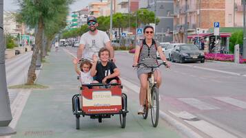 A family on a street with a child in a wagon and an adult on a bicycle.