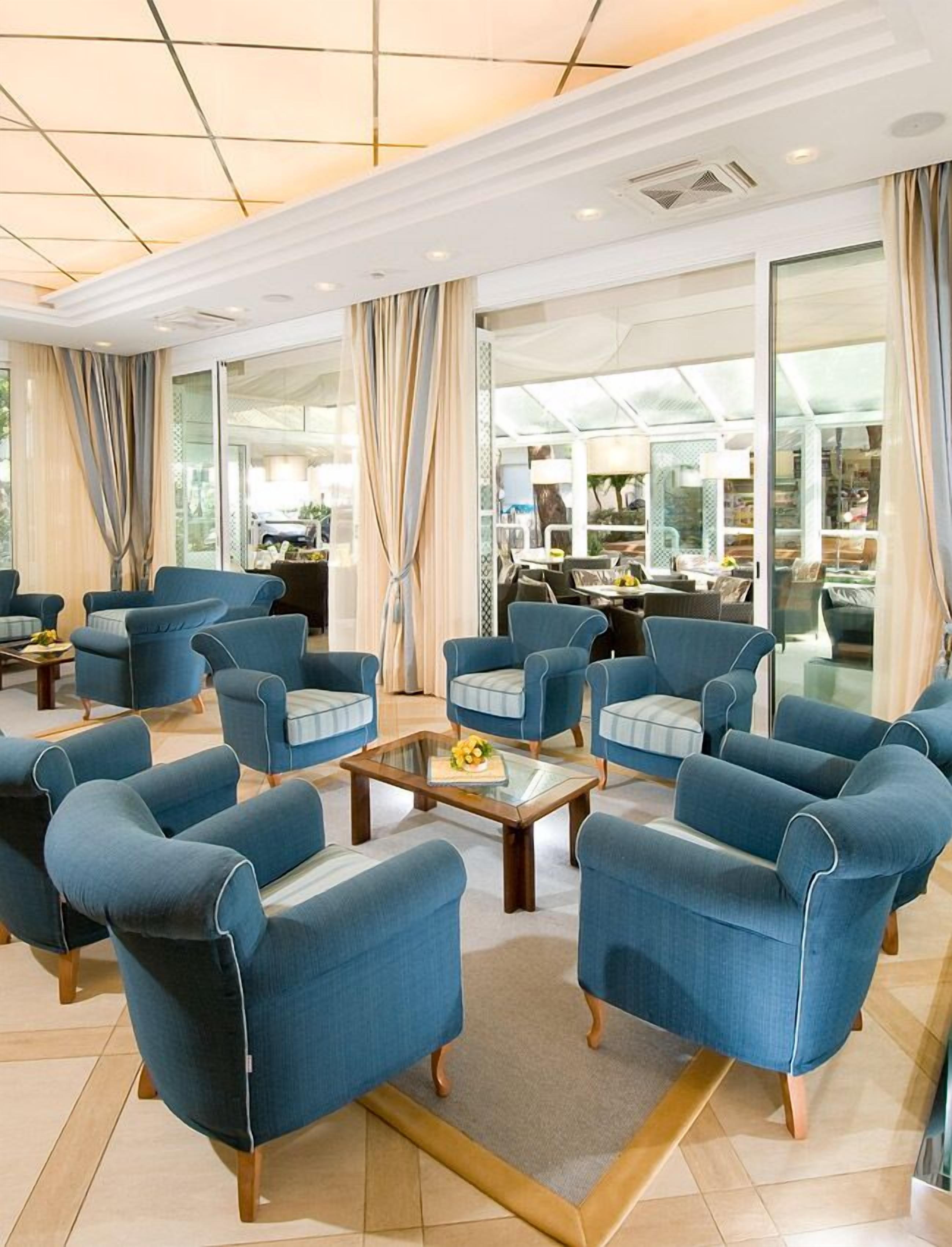 Un amplio vestíbulo con sillones azules dispuestos alrededor de una mesa de centro, ventanas grandes y vistas al área exterior.