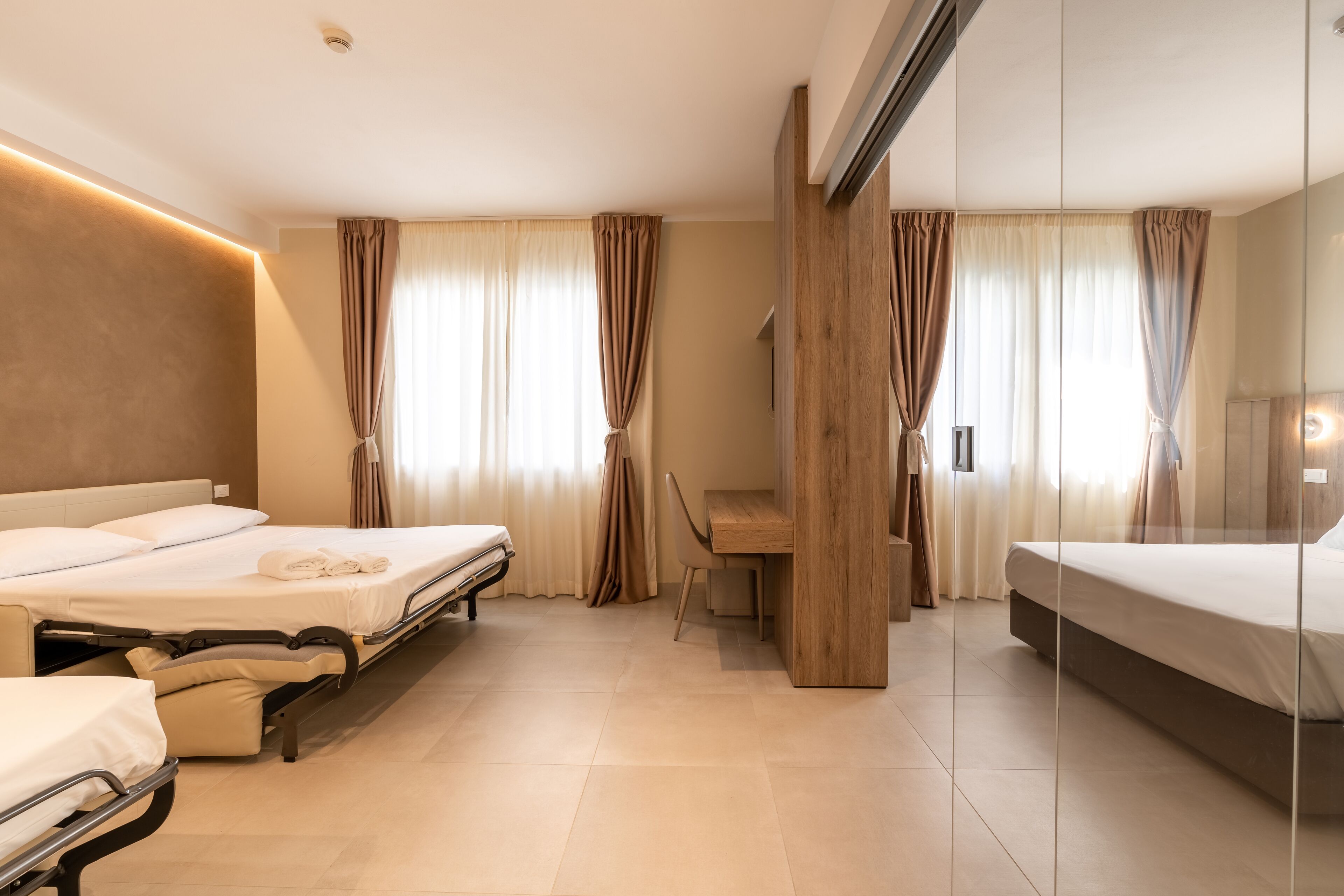 A hotel room with two beds, a wooden desk, and a large mirror.