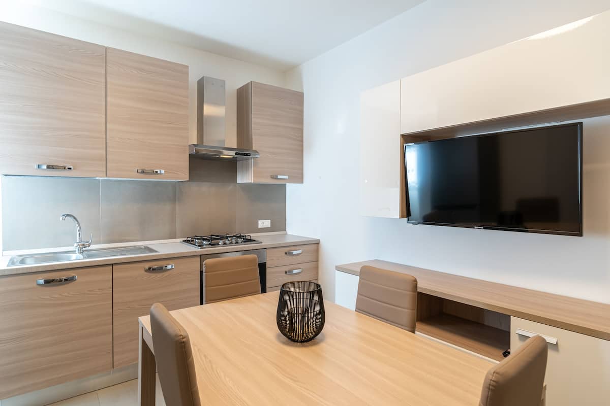 A modern kitchen with wooden cabinets, a built-in stove, a sink, and a flat-screen TV mounted on the wall.