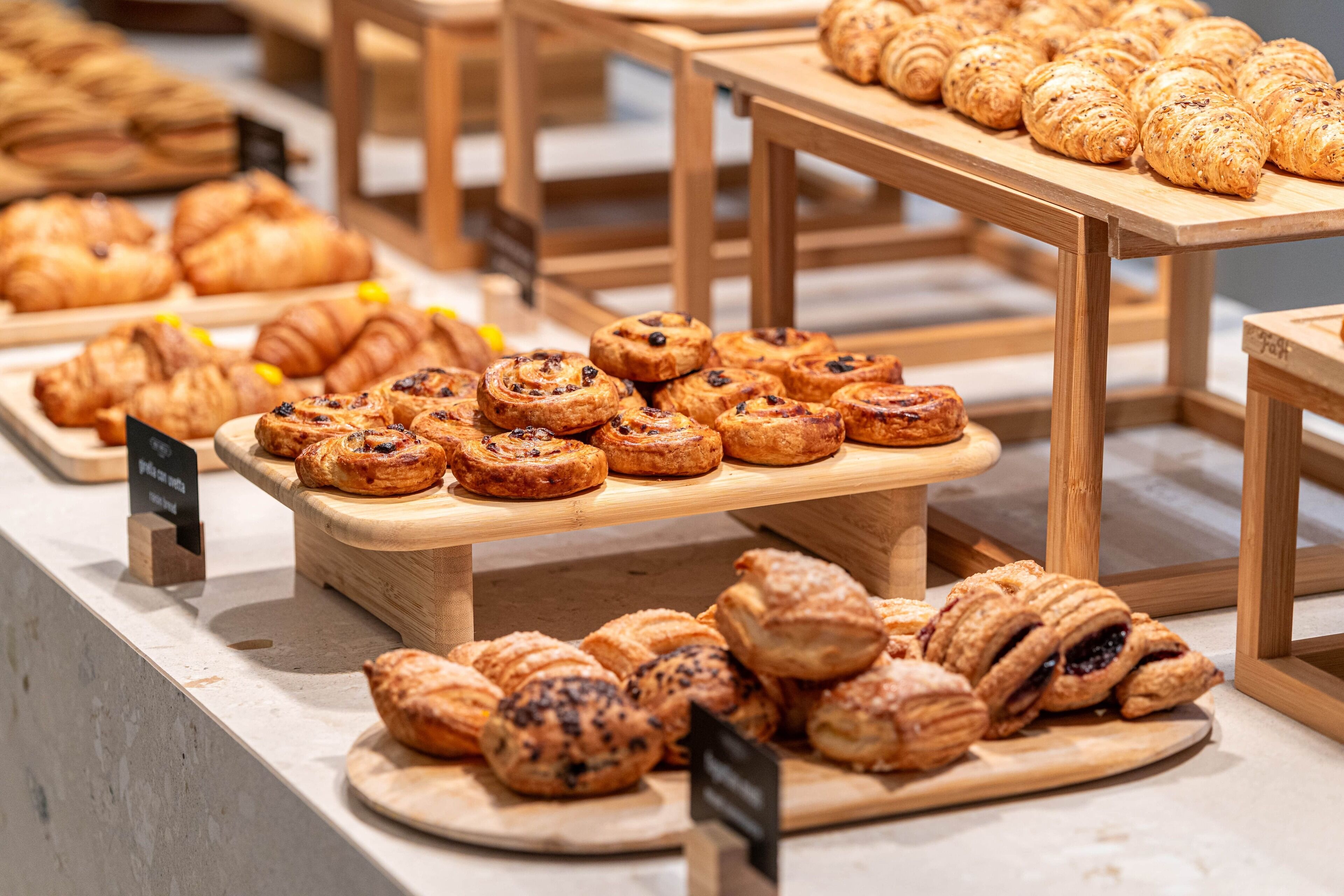 Una vitrina de pastelería con diversos tipos de productos horneados sobre pedestales de madera.