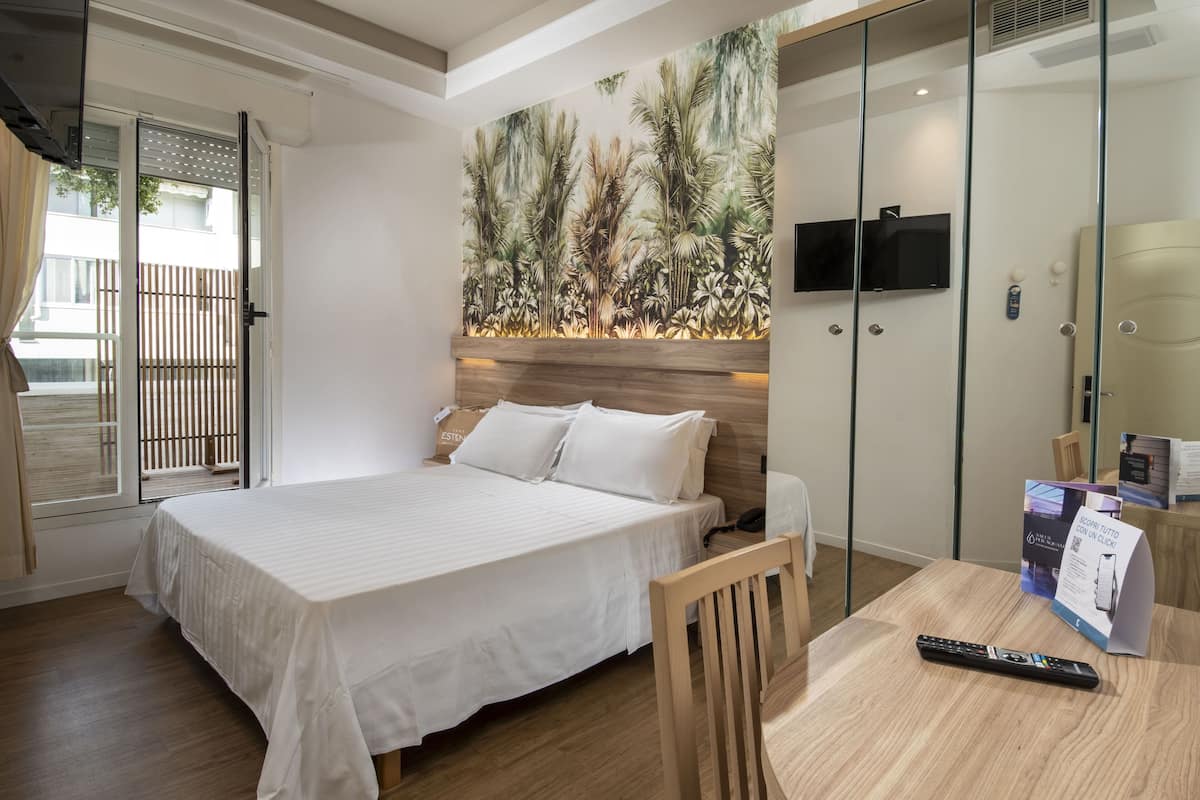 A hotel room with a bed, a TV mounted on the wall, a wooden table, and a remote control.