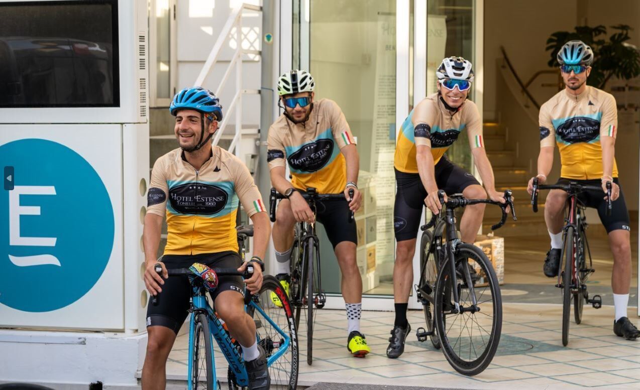 A group of cyclists in cycling attire near a building entrance.