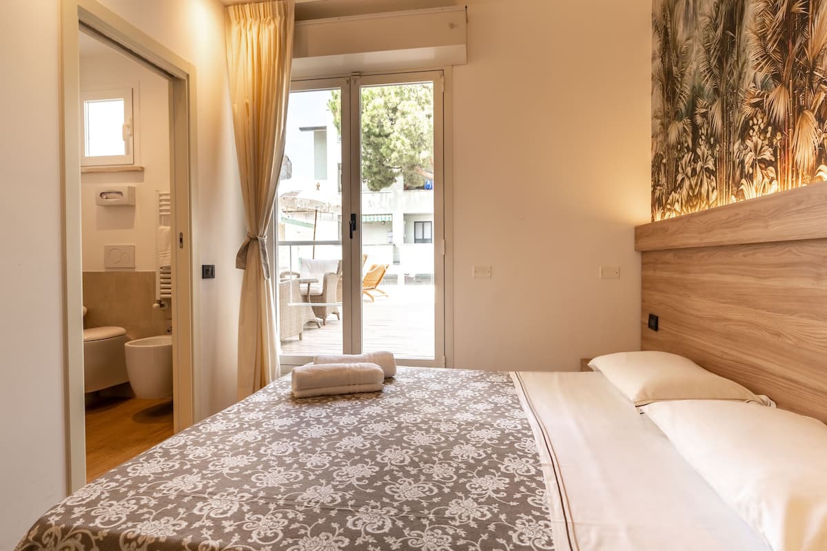 A bedroom with a bed, a bathroom, and a view of the outside.