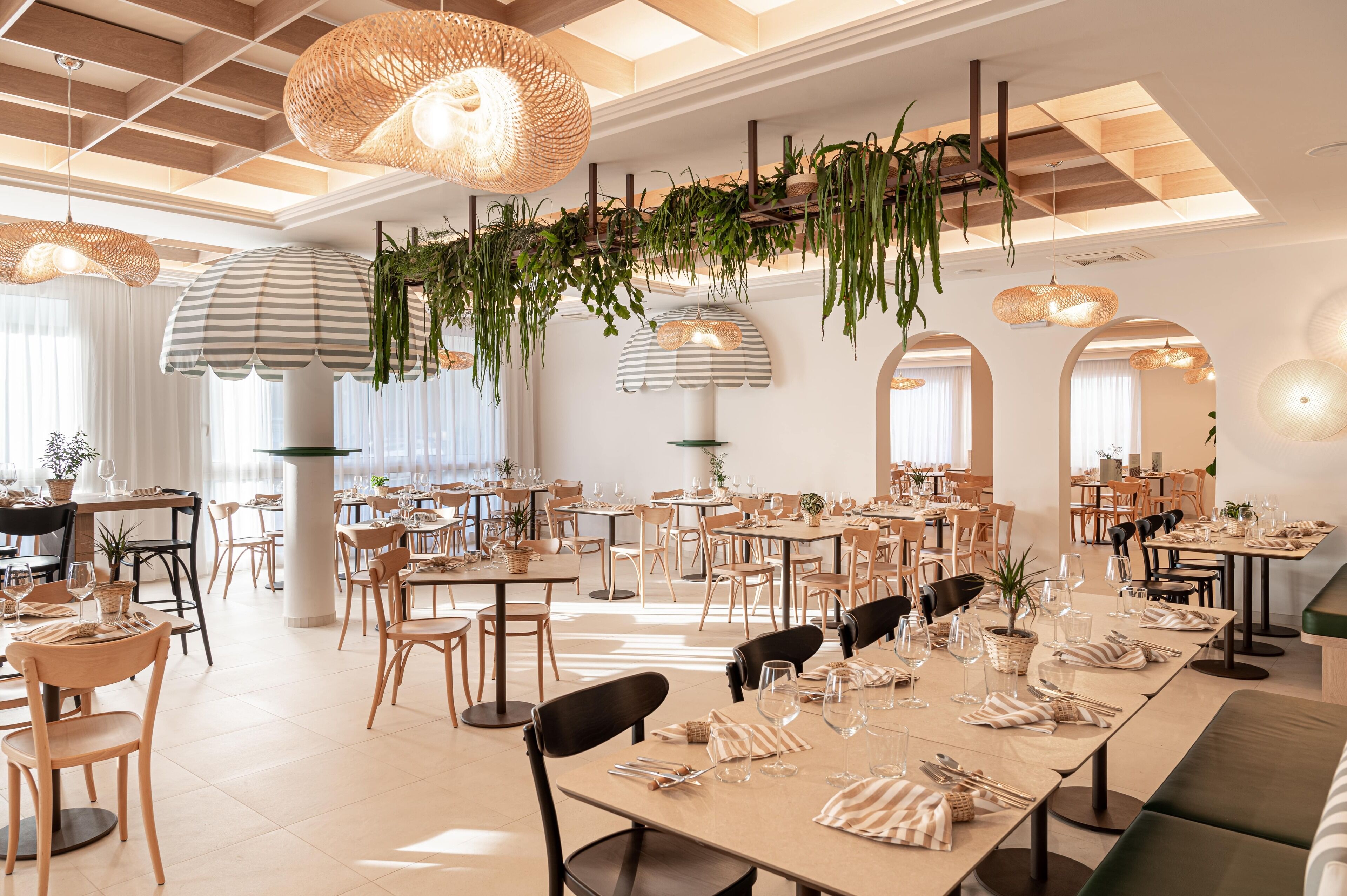 A spacious dining area with multiple tables and chairs, hanging plants, and pendant lights.