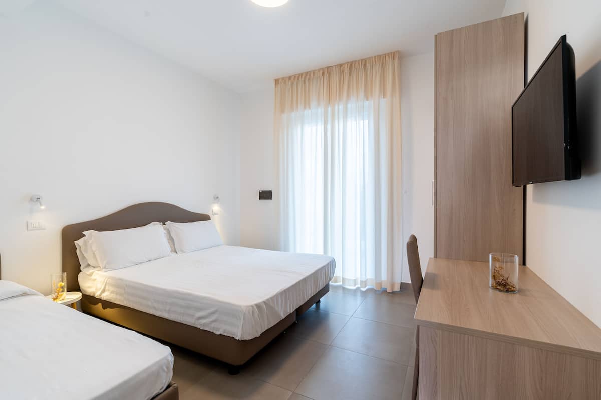A hotel room with two beds, a desk, a TV, and a window with curtains.