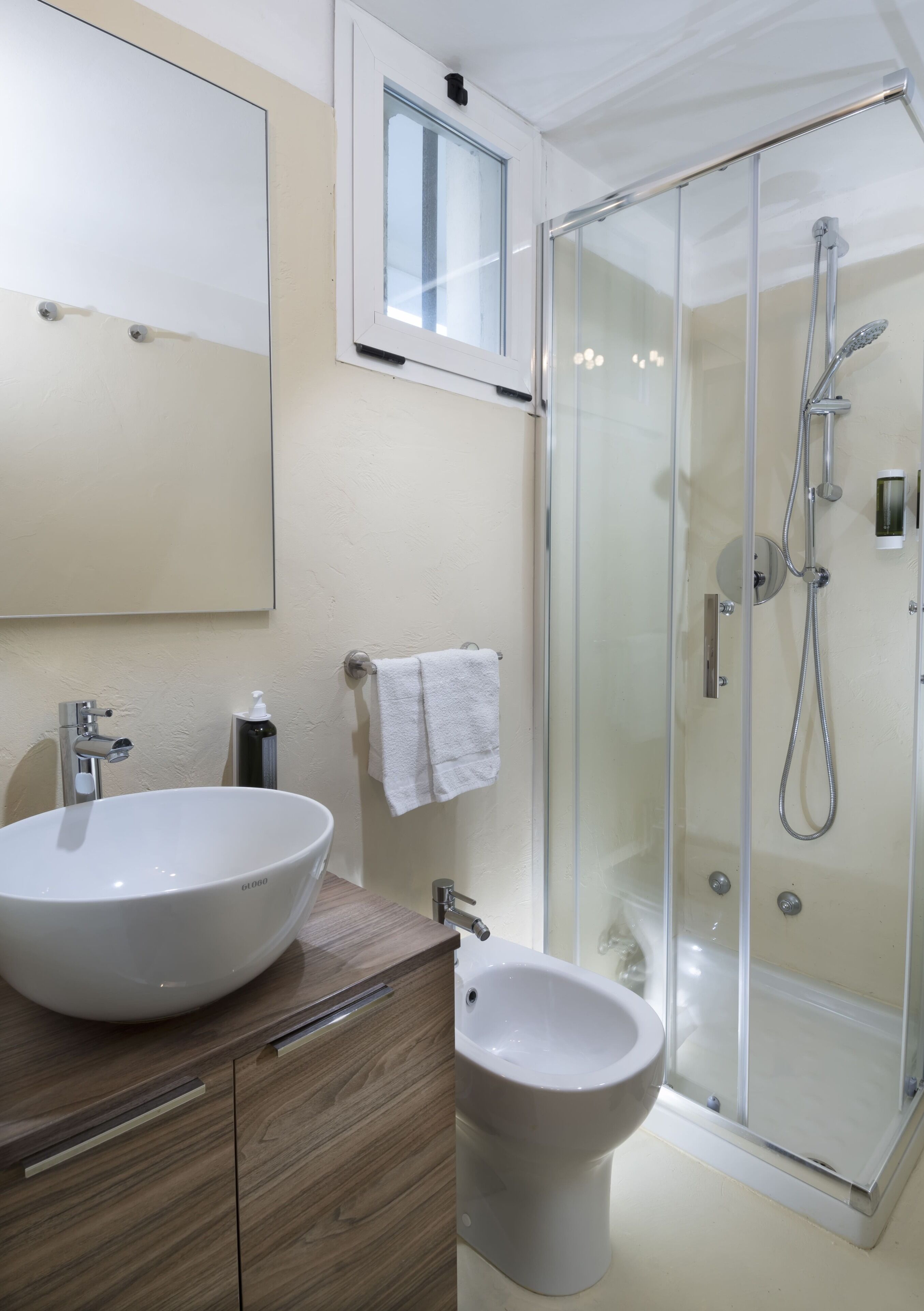 Une salle de bain moderne avec un grand lavabo blanc, un bidet, une douche à parois de verre et un miroir au-dessus du lavabo.