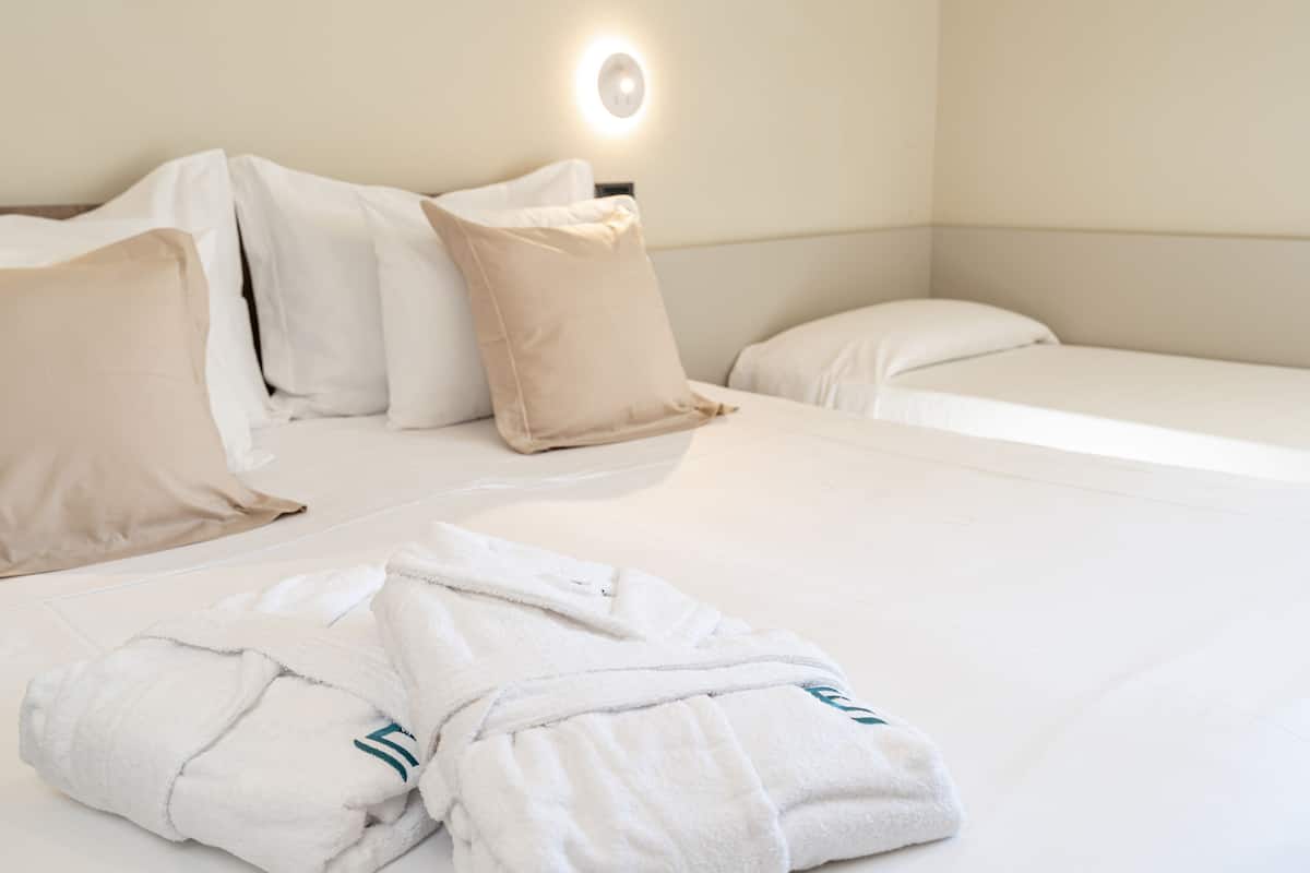 A hotel room with a neatly made bed, a bedside table, and a wall-mounted light.