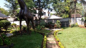 A garden with a stone pathway, a wooden bench, and a dining area with chairs and a table. - Twiga Sanctuary Resort (Kisumu)