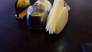 A table with a vase of flowers, a salt and pepper shaker, a napkin holder, and a number sign. - Twiga Sanctuary Resort (Kisumu)