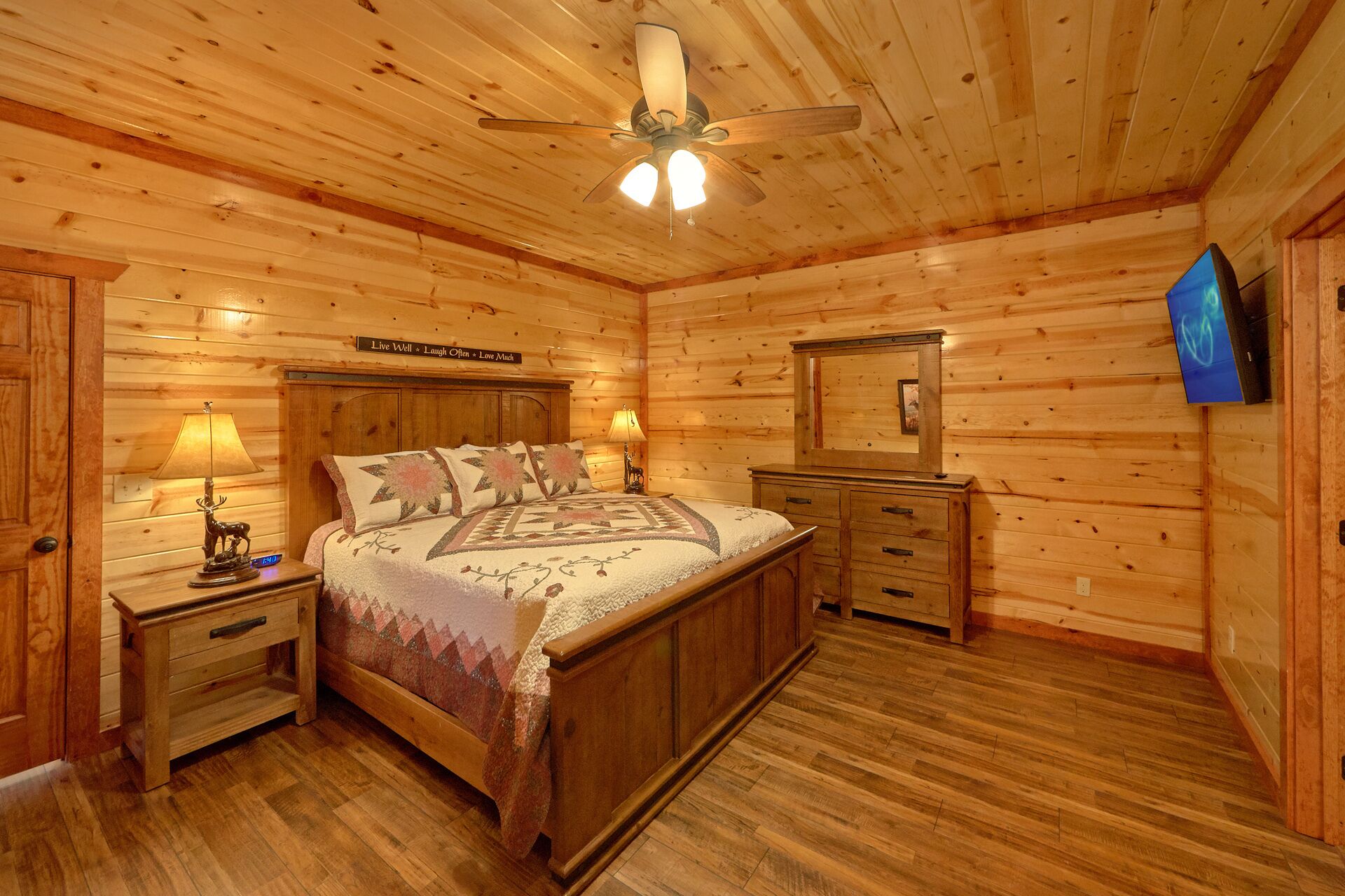 Een slaapkamer in een houten chalet, met een bed, nachtkastjes, een dressoir en een plafondventilator.