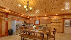 A wooden cabin interior with a dining table, chairs, a refrigerator, a microwave, and a coffee station.