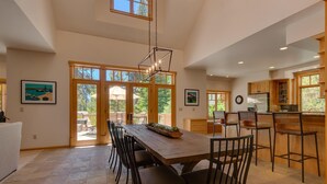 Una cocina amplia con una gran mesa de madera y sillas, una lámpara colgante y vistas al exterior a través de amplios puertas corredizas de vidrio.