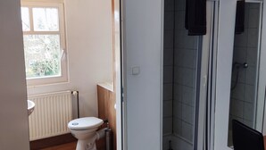 Een badkamer met toilet, douche en raam.