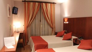 Camera d'albergo con due letti, una scrivania con lampada, TV a parete e una testiera in legno.