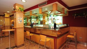 Angolo bar con banconi in legno, sgabelli e diverse bottiglie.