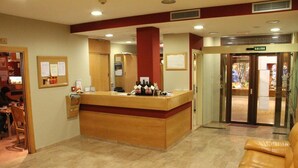 Un'area di reception di un hotel con una scrivania in legno, un divano in pelle e una porta in vetro che dà sull'uscita.