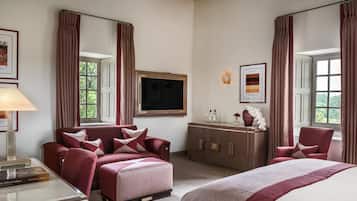 Una habitación de hotel con una cama grande, un sofá, un escritorio con lámpara, un televisor y un aparador con objetos decorativos.
