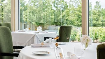 A dining table set with white tablecloths, plates, glasses, and a bottle of champagne.