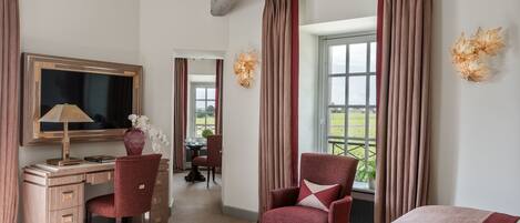 A hotel room with a desk, chair, and a bed. There is a window with curtains, a mirror, and a decorative wall piece.