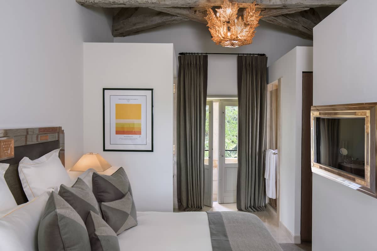 Ein Schlafzimmer mit einem Bett, einem gerahmten Bild an der Wand, einem Fenster mit Vorhängen und einer Kristallleuchter.