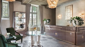 A reception area with a glass-top table, green upholstered chairs, a marble reception desk, and decorative lighting. - Château Lafaurie-Peyraguey Hôtel & Restaurant LALIQUE (Bommes)
