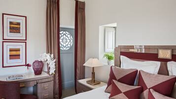 A hotel room with a bed, a desk, a lamp, and a window with curtains.