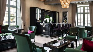 A room with green upholstered chairs, a black bar area, and large windows with curtains. - Château Lafaurie-Peyraguey Hôtel & Restaurant LALIQUE (Bommes)