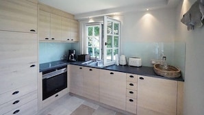 A modern kitchen with light wood cabinets, a black countertop, and a large window.