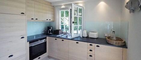A modern kitchen with light wood cabinets, a black countertop, and a large window.